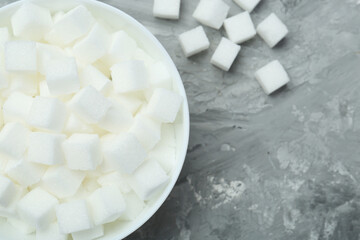 White sugar cubes in bowl on grey table, top view. Space for text