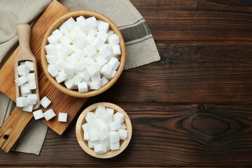 Obraz premium White sugar cubes in bowls and scoop on wooden table, flat lay. Space for text
