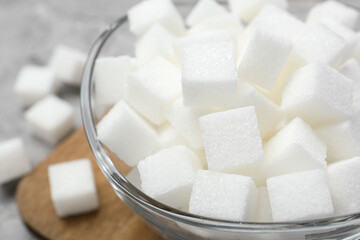 White sugar cubes in glass bowl on grey table, closeup
