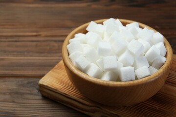 Fototapeta na wymiar White sugar cubes in bowl on wooden table, closeup. Space for text