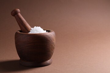 Natural salt in mortar and pestle on brown background. Space for text