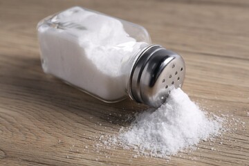 Natural salt in shaker on wooden table, closeup