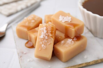 Delicious candies with sea salt and caramel sauce on white tiled table, closeup