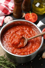 Homemade tomato sauce in pot, spoon and ingredients on dark table