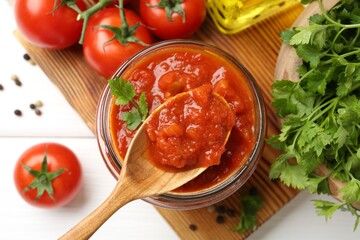 Homemade tomato sauce in jar, spoon and fresh ingredients on white wooden table, flat lay