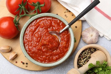 Homemade tomato sauce in bowl, spoon and fresh ingredients on light grey table, flat lay