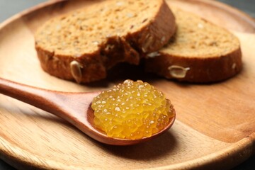 Fresh pike caviar in spoon and bread on table, closeup