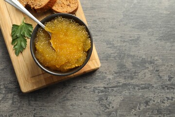 Fresh pike caviar in bowl, parsley and bread on grey table, top view. Space for text