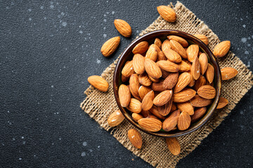 Almond nuts in bowl at black background. Top view.