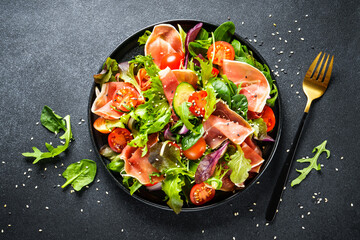 Healthy food. Fresh salad with jamon, green salad leaves and tomatoes. Top view with space for text. - obrazy, fototapety, plakaty