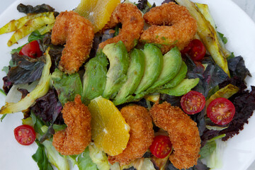 Closeup view of colorful salad with lettuce, cabbage, tomatoes, fried shrimps, avocado and orange, served on a white dish.	
