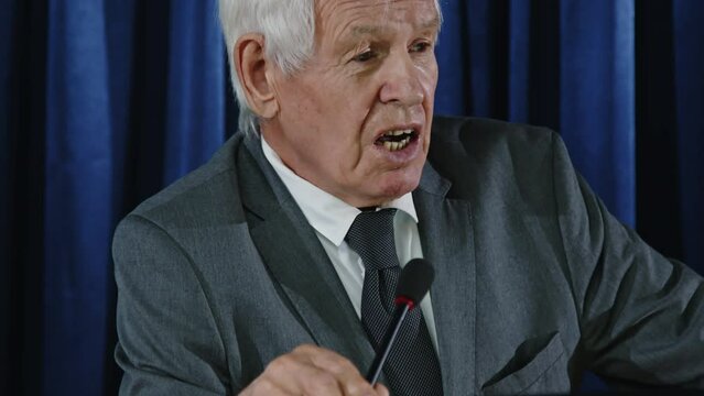 Tilt up shot of senior senator standing at lectern with microphone and giving speech during political press conference