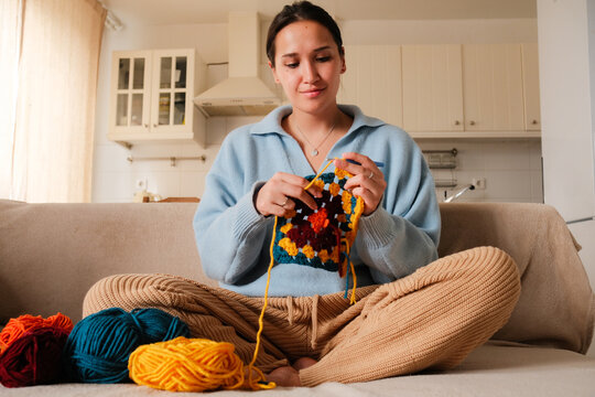 Young woman knitting crocheting with colored yarn granny square at home. Woman doing needlework, home hobbies