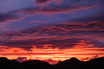 The sky is ablaze with vivid colors as the sun sets behind majestic mountains, casting a warm glow...