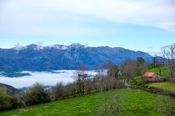 A house sits perched on top of a vibrant green hillside in the Asturias mountains of Spain, surrounded by lush greenery.