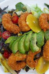 Closeup view of colorful salad with lettuce, cabbage, tomatoes, fried shrimps, avocado and orange, served on a white dish.	
