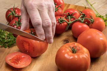 Cook hands cutting tomato slices on a wood cutting board in the kitchen
