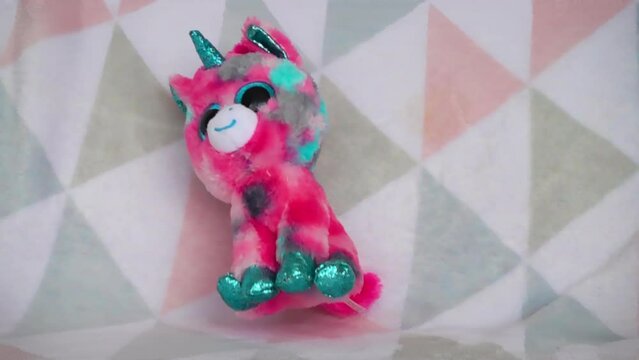 Stuffed and fluffy plush toy pink unicorn falls on a soft baby blanket. Slow motion.