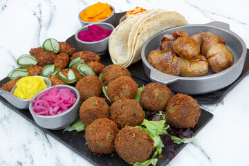 Vegan cuisine. Closeup view of fried potatoes, vegan fried kibbehs, lentil falafels, onion pickles, garbanzo, beets and carrot hummus, and corn tortillas on the white marble table.	
