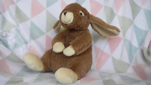 Stuffed and fluffy plush toy rabbit falls on a soft baby blanket. Slow motion.