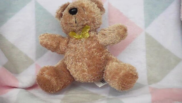 Stuffed and fluffy teddy toy brown bear falls on a soft baby blanket. Slow motion.