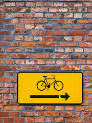 A yellow sign with a bicycle symbol painted on it is attached to a weathered brick wall. The sign indicates a designated bicycle path in a bustling urban area.
