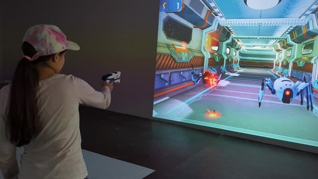 A game projection on the wall with a child opposite, using an interactive gun, enthusiastically playing shooter games.