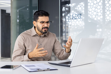 Indian businessman looking confused while gesturing during a discussion at his modern office. This image captures workplace challenge and problem-solving scenarios.