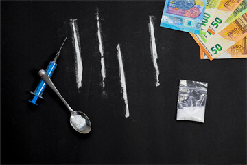 cocaine lines with syringe and spoon, bag full of heroin on blac