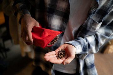 Man Pouring Roasted Coffee Beans Into His Hand From a Red Pouch Package