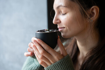 Smiling Woman Holding a Cup of Hot Drink in a Cozy Indoor Setting