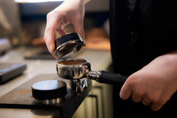 Barista Pressing Ground Coffee Into a Portafilter With a Tamper at a Cafe