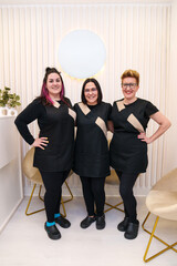 Three smiling women in chic uniforms inside a clinic.