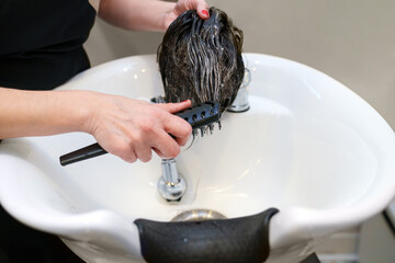 Stylist's hands rinse a hairpiece at a clinic sink.