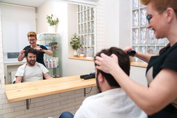 A content man observes as his hairpiece is styled by a professional.