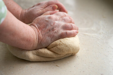 Elderly woman's hands knead dough on table. Copy space.