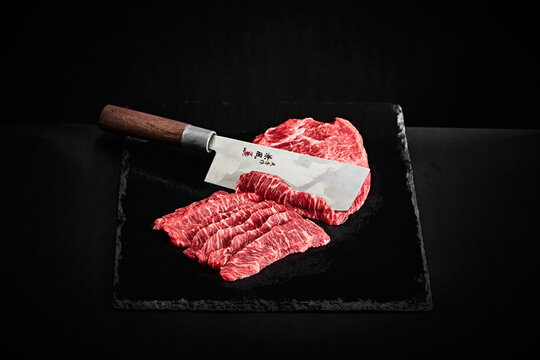 Wagyu beef slices with Japanese carving knife on black slate