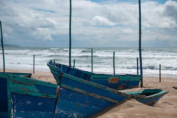 Wooden boats stranded on the beach abandoned and decrepit due to inclement weather with rough seas in the background