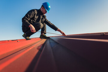 Young man worker in helmet holding meter tape on roof with blue sky. Roofer work background - 783249287
