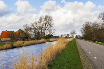 A country road in North Holland near the town of Schagen with typical Dutch houses on a polder at the edge of a drainage canal