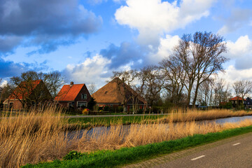 A country road in North Holland near the town of Schagen with typical Dutch houses on a polder at the edge of a drainage canal