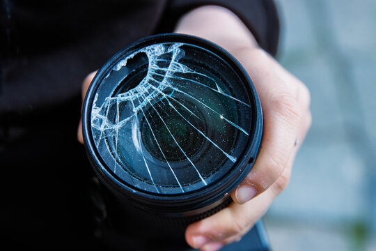 Hands of young photographer holding DSLR photo camera with  broken lens filter glass after if fall down onto the floor. Close up. Destroyed cracked photo-filter. Macro. Top view. Selective focus.