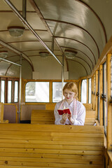Red-haired girl in an old tram. Schoolgirl in the USSR. Young woman is reading a book