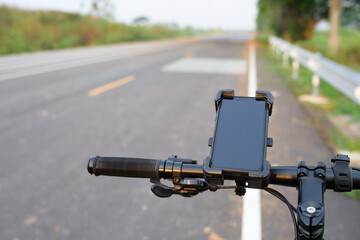 Smartphone and quick release holder attached on the handle bar of a bicycle with country road on...