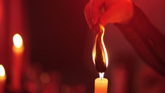 A woman's hand holds a palo santo stick in a candle flame, red light
