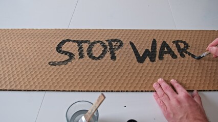 Caucasian Male Anti War Activist Preparing Banner for Political Demonstration Raid with Stop War Text Painted on Cardboard - obrazy, fototapety, plakaty