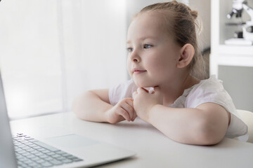 Cute little girl using laptop at home. Education, online study, home studying The girl at home communicates with friends on the Internet. Kids distance learning. High quality photo