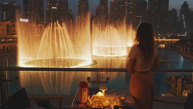 video with noise. Dark blurred silhouette of woman tourist back rear view. Girl stands on balcony enjoy admires view beauty night city downtown Dubai United Arab Emirates. Warm orange light lights 