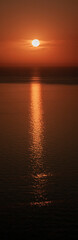 Sunset over the sea against the background of the coast. Evening on the sea calm in clear weather. The disk of the sun in the evening sky over the sea.