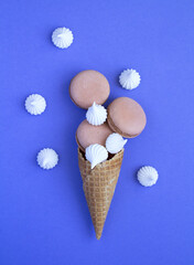 Ice cream cone with chocolate macaron and white meringue on the purple background. Top view.Location vertical.
